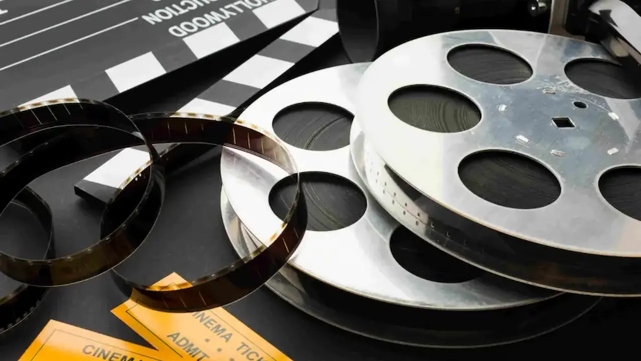 Rolos de filmes de cinema com dois ingressos  e um claquete em cima de uma mesa