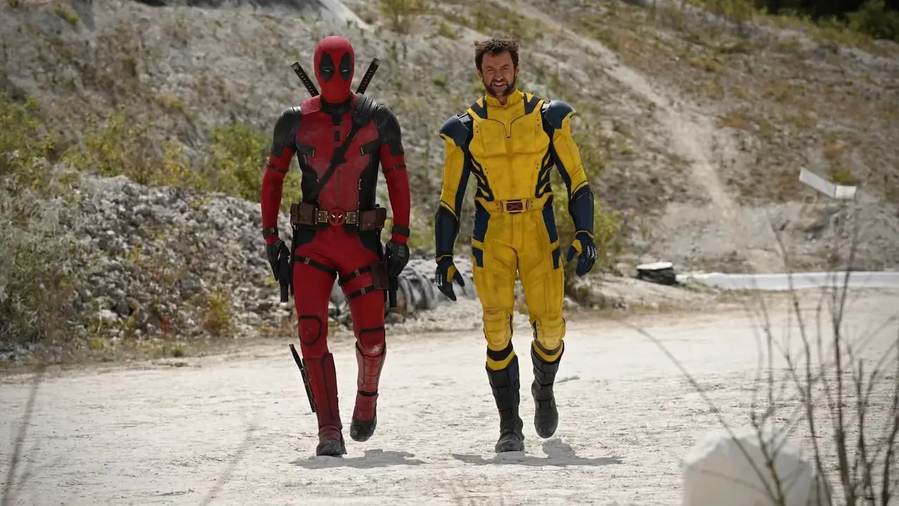 Deadpool com seu traje vermelho e Wolverine com seu traje amarelo andando lado a lado em um local desolado