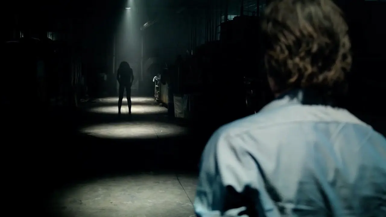 um homem em um corredor escuro com uma figura sinistra sob uma luz