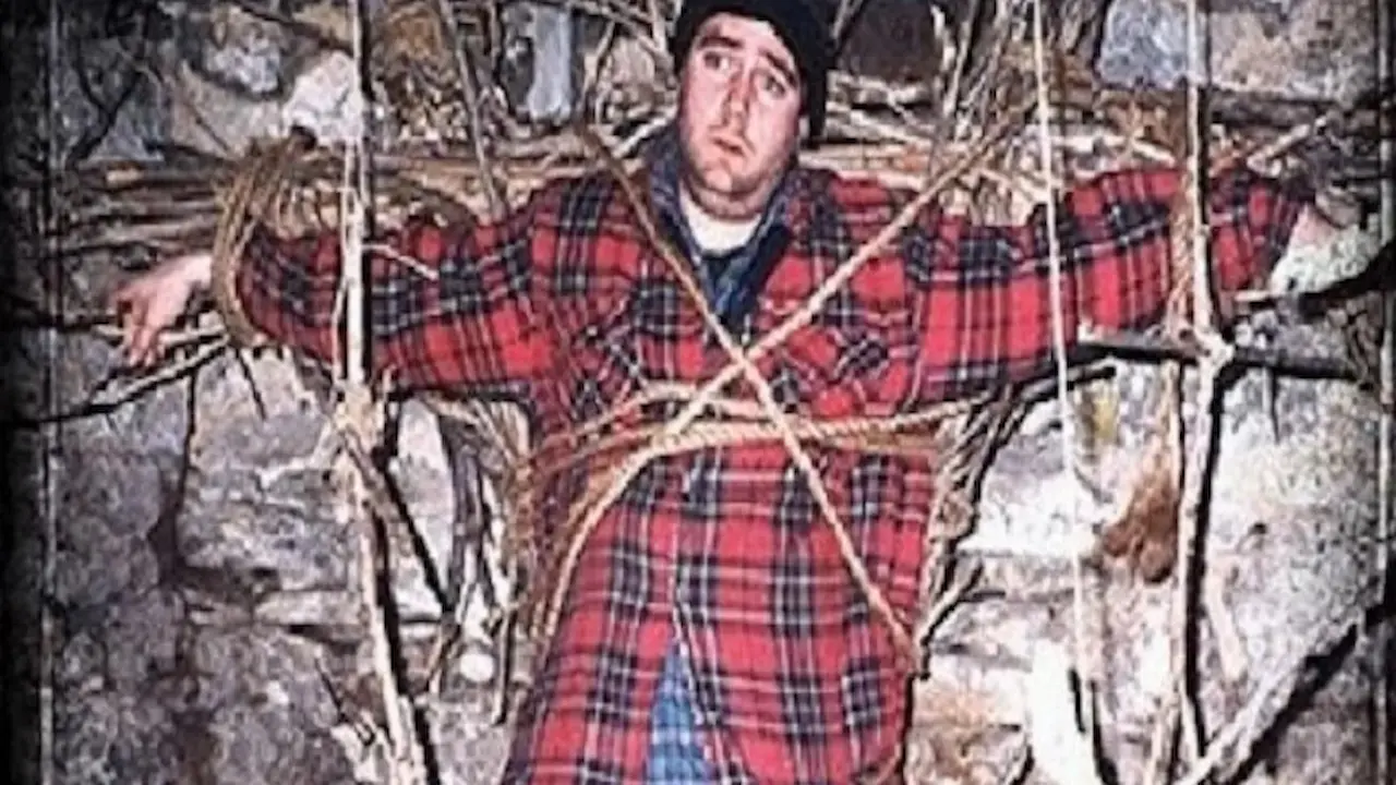Homem acima do peso com camisa vermelha amarrado em um ritual de bruxa em uma caverna