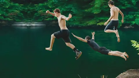 três jovens pulando do alto de uma pedra em um lago de cachoeira no meio da floresta